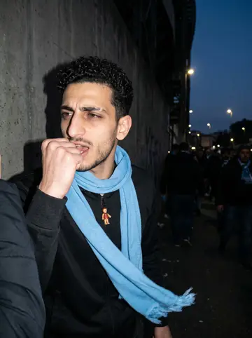 Renzo, AI character: outside the Maradona stadium in Naples after a Napoli match, fans streaming behind him in the dark