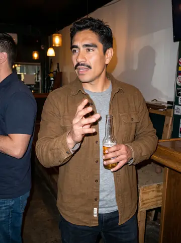 Camilo, AI character: a Colombian tejo club in Corona on a Sunday night, wooden bar and a tejo lane behind him, another man's…