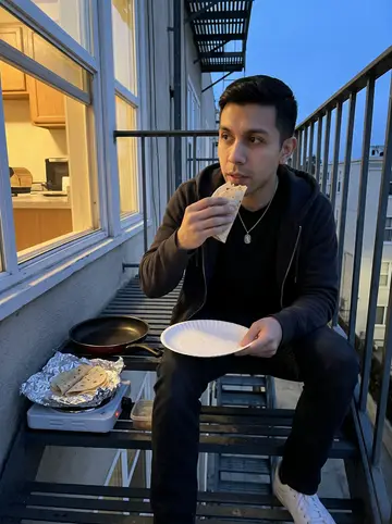 Emiliano, AI character: the metal fire escape outside his apartment window in San Diego at dusk, a small hot plate with a pan of…