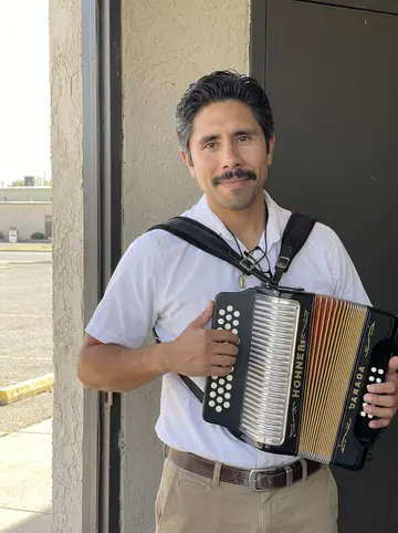 Benicio, AI character: outside the VFW hall on Zapata Highway before the Sunday conjunto set, standing by the side door with his…