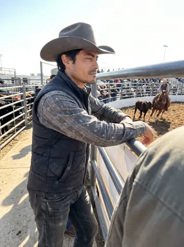 Beto, AI character: beside the cutting-horse arena at the Fort Worth Stock Show, steel rails and livestock pens behind him,…