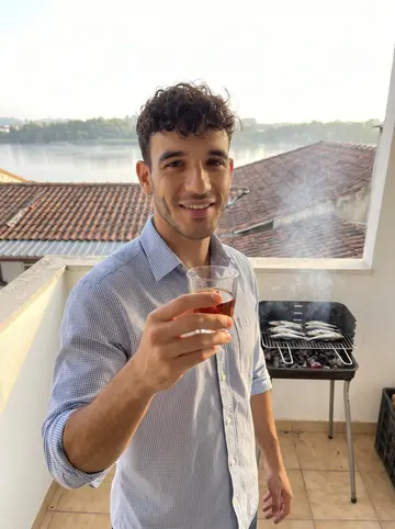 Joao, AI character: his narrow balcony in Miragaia on a Saturday evening, a small charcoal grill with sardines behind him,…