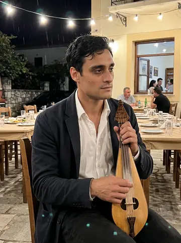 Yorgos, AI character: the village square in Anogeia on a warm feast night, long tables and strings of bulbs, people blurred…