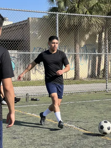 Jerónimo, AI character: small neighborhood soccer court in Little Havana on a bright spring afternoon