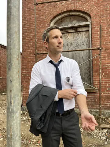 Archer, AI character: outside an old red-brick mill building in Providence during a site walk, scaffolding poles and a boarded…