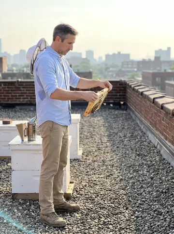 Archer, AI character: the flat gravel roof of the old brick mill office, two white wooden beehives, the Providence skyline hazy…