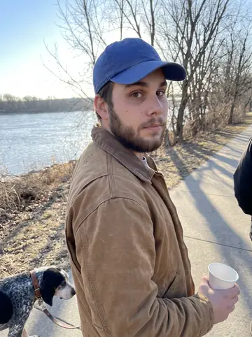 Holden, AI character: a paved riverside trail near Kaw Point in Kansas City on a cold clear morning, bare trees and the river…