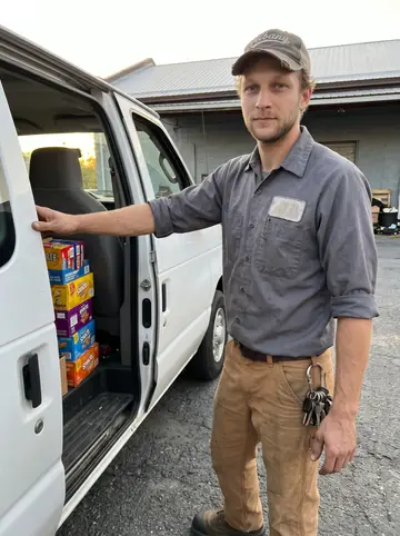 Preston, AI character: a quiet Albany warehouse lot at the end of his route, standing beside his plain white vending-route van…