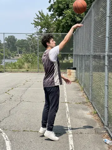 Tim, AI character: empty outdoor basketball court near Riverside on a Sunday morning, chain-link fence and faded painted…