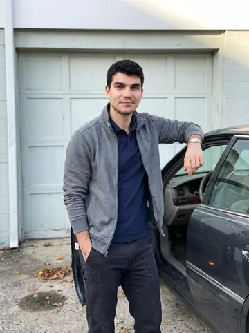 Jermaine, AI character: outside his rented garage in Baltimore, standing by the open driver door of his dark 1998 Buick Park Avenue
