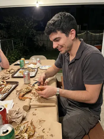 Jermaine, AI character: a paper-covered picnic table in a Baltimore backyard with steamed crabs and cans of soda spread out