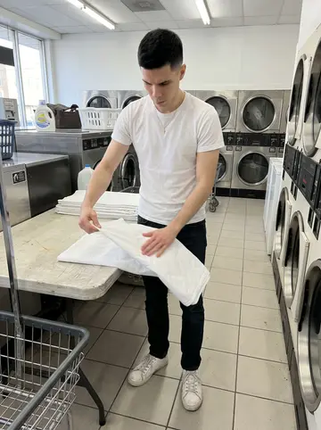 Leon, AI character: inside one of his Newark laundromats on a quiet weekday morning, folding table between two rows of dryers
