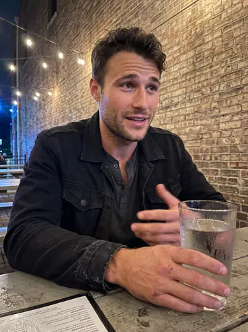 Derrick, AI character: a casual Tremont patio bar after work, brick wall and string lights behind him