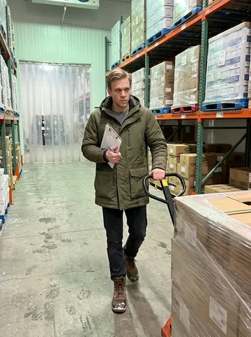 Jelle, AI character: inside the cold-storage warehouse in Grand Rapids, between tall freezer racks and wrapped pallets