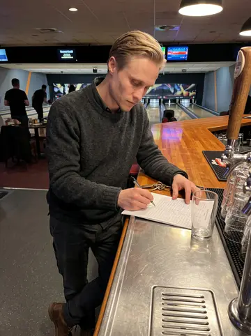 Arttu, AI character: behind the bar at the bowling alley during Tuesday league night, scoring sheets and beer taps in the…