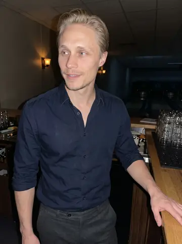 Arttu, AI character: at the end of the bowling alley bar after closing, dark lanes behind him and stacked glasses on the counter