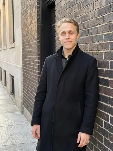 Emil, AI character: Benefit Street in Providence at late afternoon, leaning against a dark brick wall outside a wedding venue…