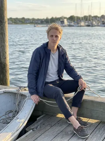 Emil, AI character: Narragansett Bay beside his battered secondhand dinghy pulled up near the dock after an evening sail