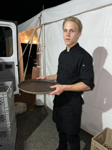 Emil, AI character: behind a Newport wedding tent at night, near the catering van and stacked crates after dinner service
