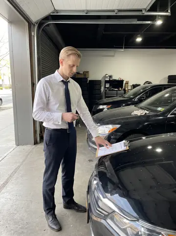 Torstein, AI character: the limousine company garage in Brooklyn, black cars lined up with a clipboard on the hood of the nearest…