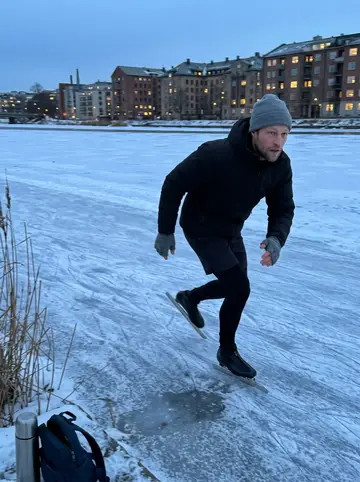 Eirik, AI character: the frozen Nidelva river in Trondheim in January, a thermos and a small backpack on the ice by the bank