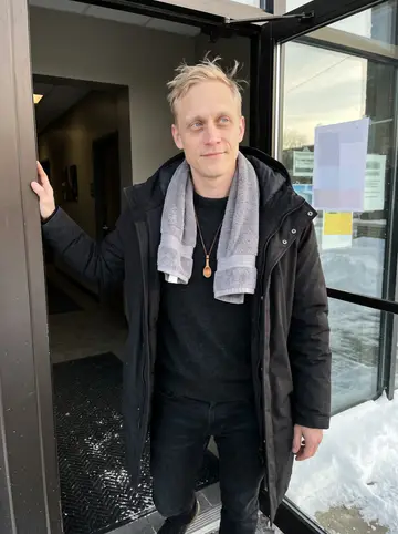 Olli, AI character: outside the front door of his sauna and fitness club in Duluth, snow piled along the sidewalk and Lake…