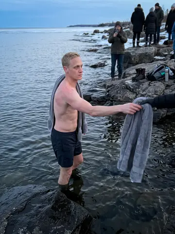 Olli, AI character: the rocky shore of Lake Superior after an ice swim, blue evening over the water and a small group of…
