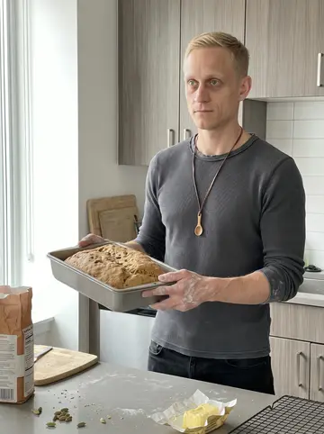 Olli, AI character: his apartment kitchen above the club, flour on the counter and cardamom bread cooling unevenly in a metal pan