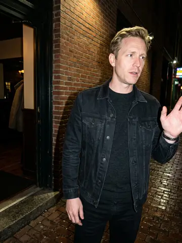 Olli, AI character: outside a Canal Park bar after a late league game, wet pavement and a brick wall behind him
