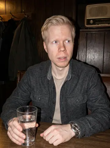 Petri, AI character: a small Duluth neighborhood bar after a winter hockey game on the radio, dark wood wall and coats on hooks…