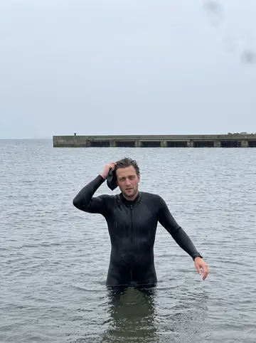 Nils, AI character: the Öresund shoreline near Malmö in October, grey water around his waist and a low pier behind him