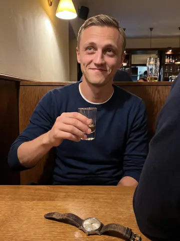 Oleksiy, AI character: a small Vienna bar after a family dinner, warm wood table and blurred relatives' shoulders around him