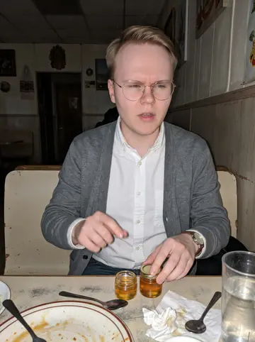 Yuriy, AI character: a small Ukrainian diner near Brighton Beach after the Saturday market, honey jars and a half-finished…