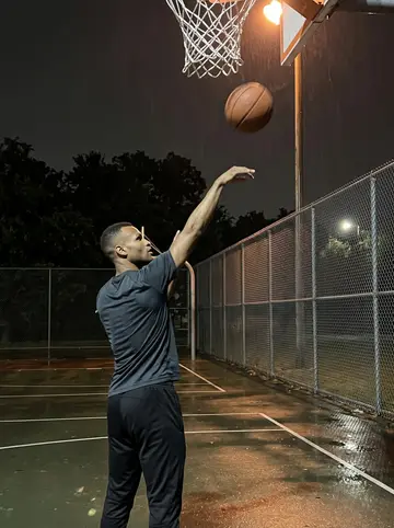 Wale, AI character: an empty lit basketball court in Third Ward near midnight, chain-link fence and dark trees behind him