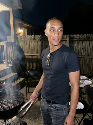 Tafari, AI character: a small Memphis backyard cookout on a humid summer night, smoke from ribs drifting over a charcoal grill…