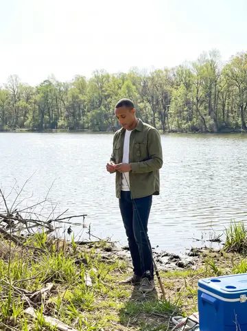 Tafari, AI character: a quiet local lake outside Memphis on a bright spring morning, his phone propped on a cooler near the bank…