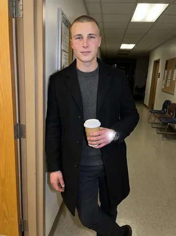 Elias, AI character: a community college adult education hallway on GED exam night, standing near a plain classroom doorway…
