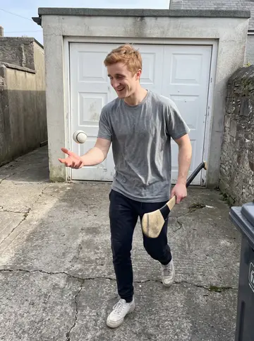 Fergal, AI character: the concrete yard of a terraced house in Cork on a Sunday afternoon, a garage door with a painted white…