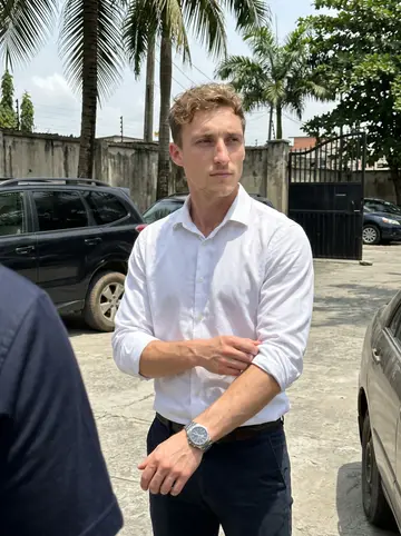 Brendan, AI character: beside a black SUV inside a gated compound in Port Harcourt, Nigeria, palm trees and a concrete wall behind