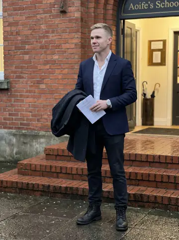 Hugh, AI character: outside Aoife's school after an evening fundraiser, wet pavement and brick school steps behind him