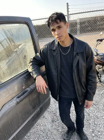 Alfredo, AI character: outside the San Antonio impound lot gate near a dusty tow truck and his father's parked 1998 Harley Sportster