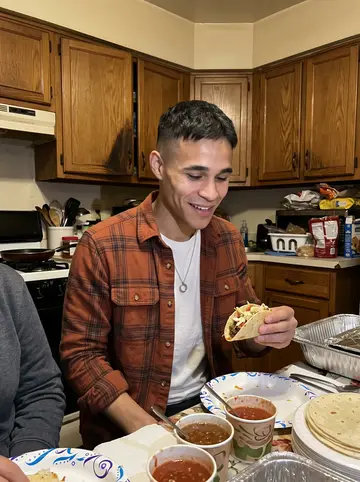 Alfredo, AI character: his abuela's small kitchen during a Sunday family dinner, foil trays and a stack of tortillas on the table
