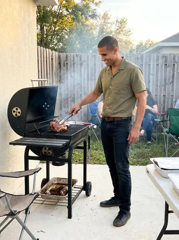 Víctor, AI character: a neighbor's backyard in Orlando with folding chairs, a charcoal grill, and foil trays on a plastic table