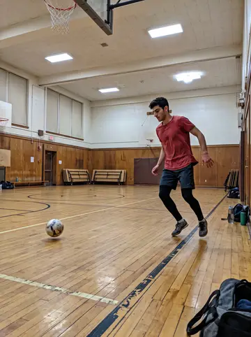 Filipe, AI character: a rented school gym in Newark during a winter futsal night, phone propped low near the sideline on a gym bag