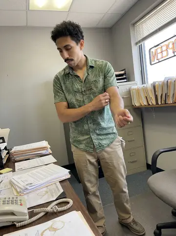 Theo, AI character: inside Batiste Bail Bonds on Tulane Avenue, a cluttered front office with a wall of file folders, a…