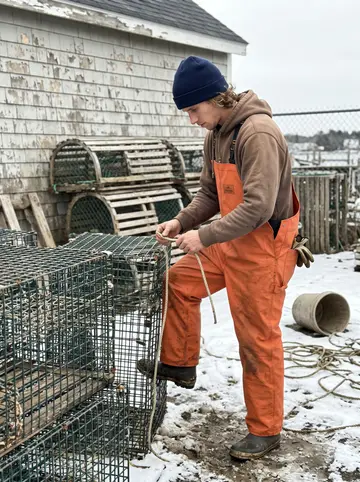 Lane, AI character: the open trap yard beside his grandfather's weathered bait shed in Stonington, a thin crust of old snow…