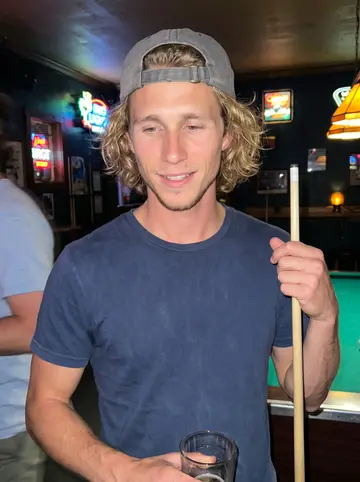 Lane, AI character: the harbor bar in Stonington on a humid summer night, a pool table with a green felt behind him and neon…