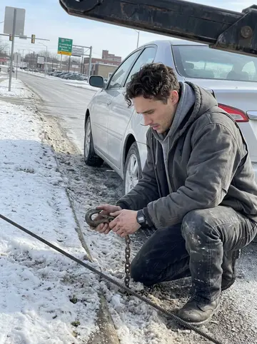 Edwin, AI character: a salted curb lane on Cleveland's east side, his tow truck angled behind a stalled silver sedan