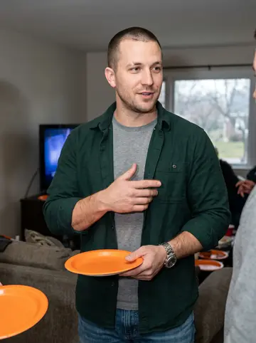 Keith, AI character: his sister's Cleveland living room during a Browns Sunday, orange paper plates and a TV glow behind him