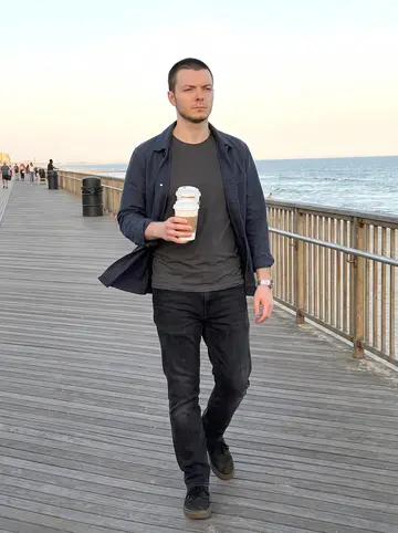 Lucas, AI character: Rockaway boardwalk on a Sunday near the railings, ocean and low sun behind him